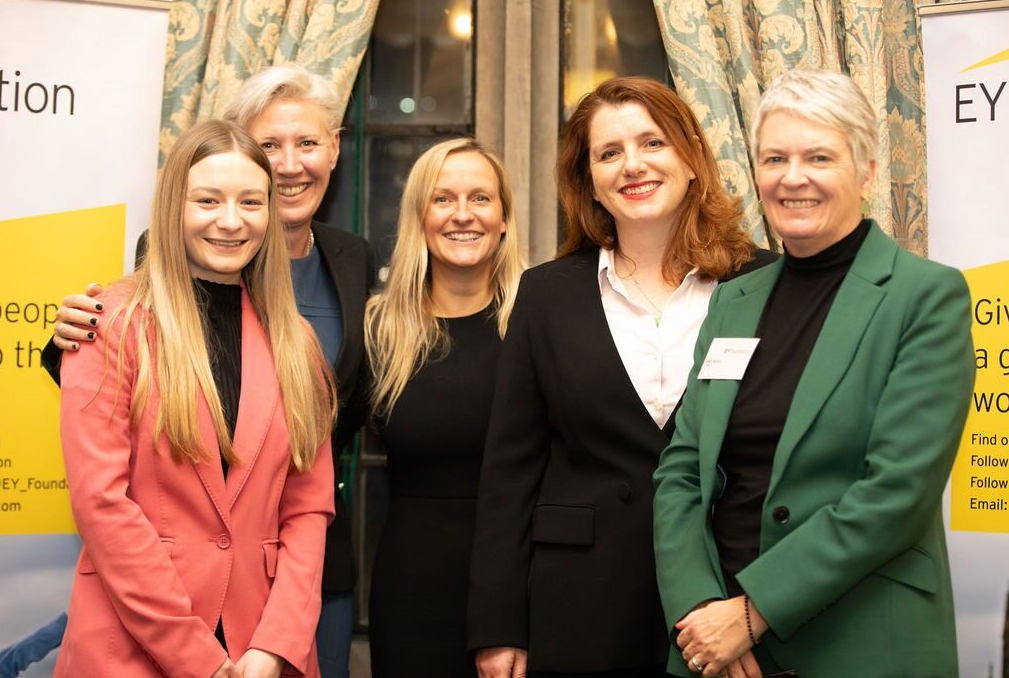 Five people stand on a podium in the Houses of Parliament.