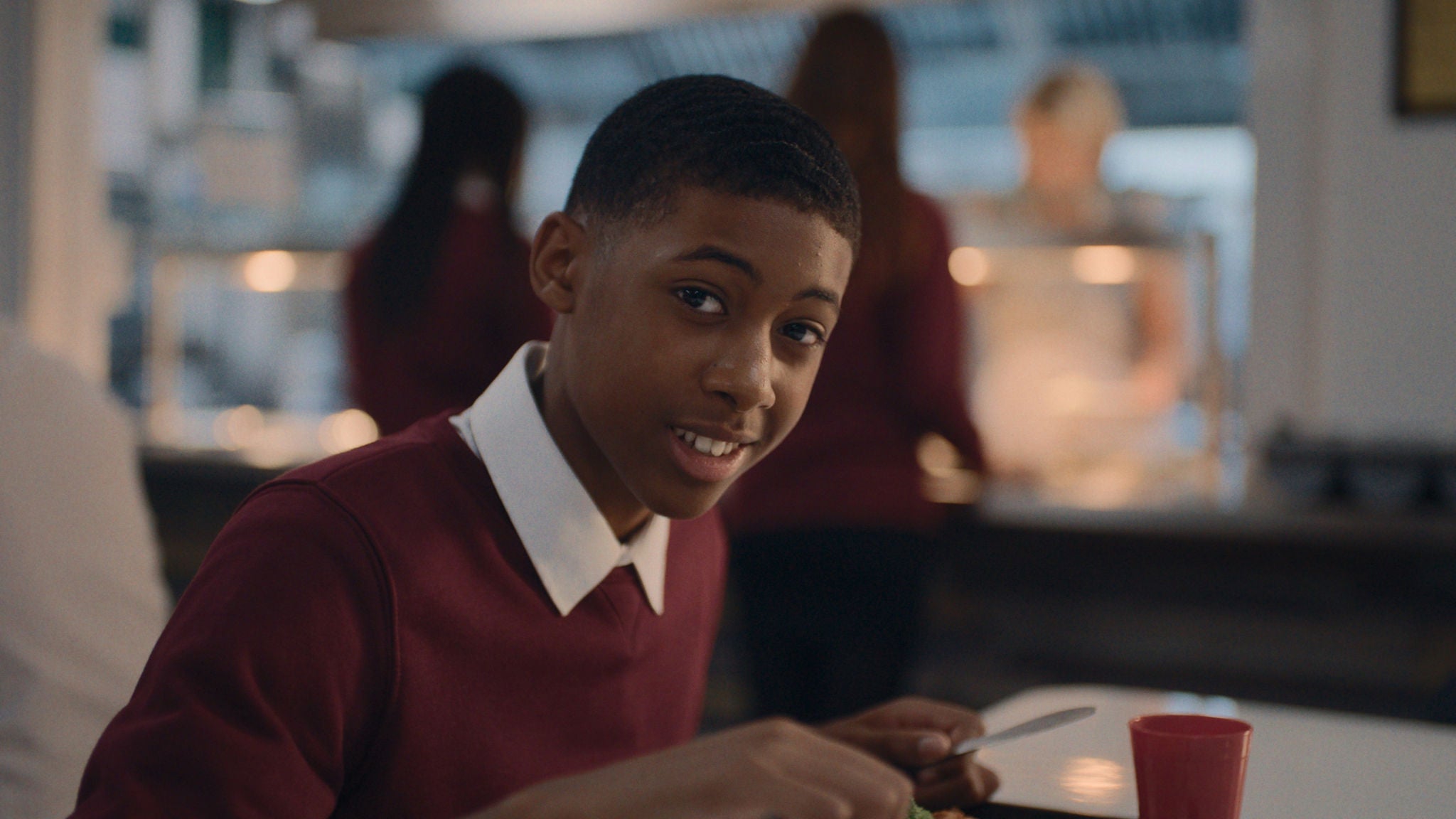 Young man in a school canteen looks at the camera in his uniform.