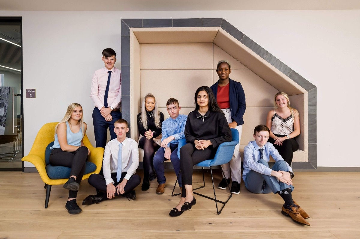 Three young people from the EY Foundation programmes are sat together on a bench.