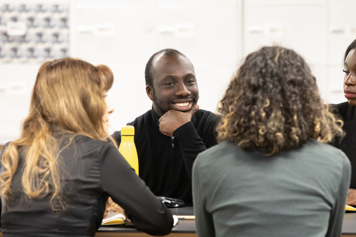 Elijah is smiling sat with a group of young people on a table with two people's backs to the camera.