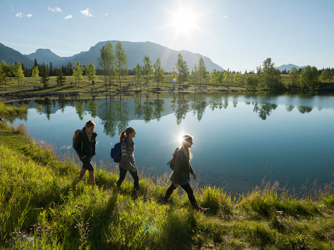 Three hikers walk along shore of mountain lake - stock photo